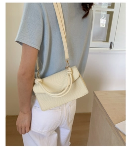 Gros plan d'un sac à bandoulière tressé crème porté par un mannequin au style minimaliste