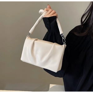 Close-up of beige ruched dumpling bag with chunky leather handle and silver buckles