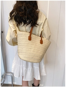 Detail view of large straw tote bag with brown straps worn by a model for beach vacation