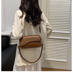 Sacoche marron vintage avec large bandoulière et chaîne porté sur un blazer blanc