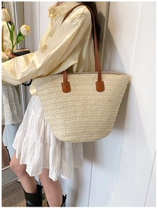 Detailed close-up of large straw tote bag with brown faux leather straps for summer beach