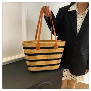Close-up of woven tote bag featuring khaki and black stripes and brown leather strap details