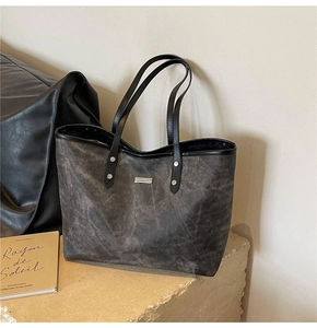 Close-up of a dark grey tote bag with black handles and metallic brand logo detailing