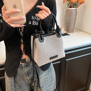 Minimalist canvas straw bucket bag with black leather trim and elegant knotted handle