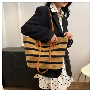 Detail of woven striped tote bag with brown leather handles worn by a model