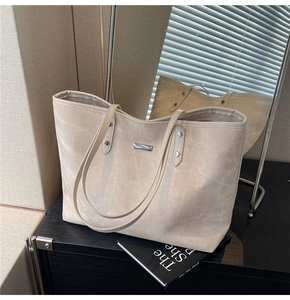 Detail of beige tote bag with silver metal plaque and reinforced rivets on black surface