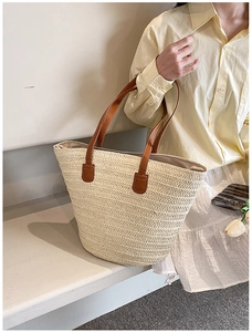 Detailed view of the woven straw texture and premium brown leather handles on the tote bag
