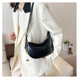 Detail of minimalist black PU leather dumpling bag with adjustable strap and gold metal zipper