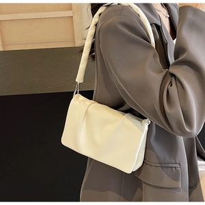 Detail of a creamy white pleated crossbody bag with thick padded strap and silver hardware