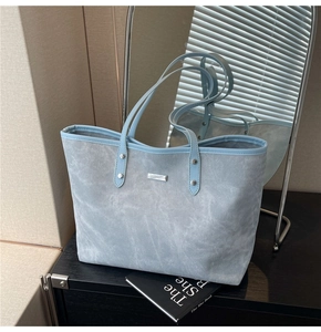 Detail of light blue textured tote bag with metal nameplate and smooth leather trim