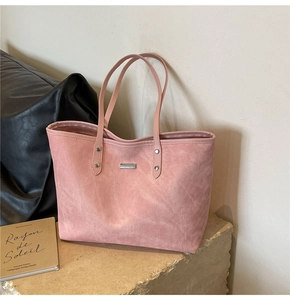 Detail view of pink suede tote bag with silver logo plaque on textured stone surface