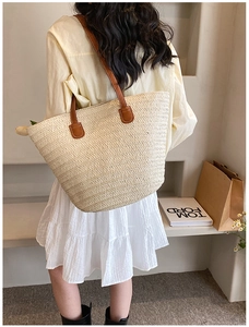 Detail of a large cream woven straw tote bag featuring contrast brown leather shoulder straps