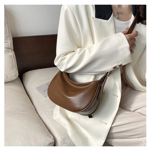 Detailed view of caramel brown leather dumpling bag worn with a white casual suit