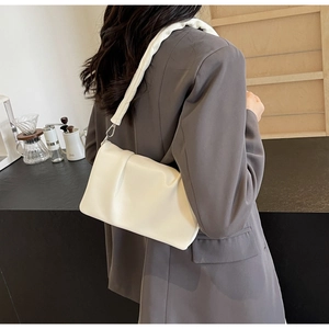 Close-up of white ruched shoulder bag with metallic buckle and soft pleated strap detail