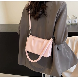 Detail of pink pleated crossbody bag with chunky cloud handle and slim strap on grey suit