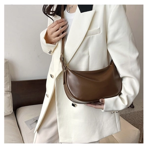 Detail view of a dark brown PU leather half-moon bag on a model in a white suit