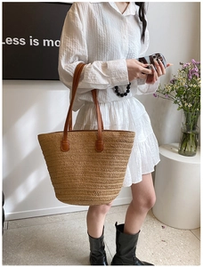 Detail of hand-woven straw tote bag with brown leather handles and reinforced stitching