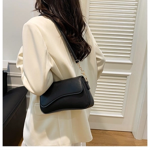 Détail d'un sac bandoulière noir avec rabat ondulé porté sur un blazer crème chic