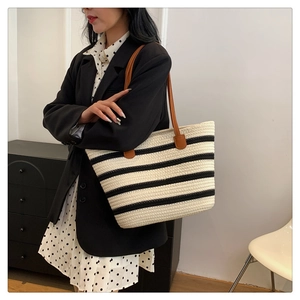 Detail of woven striped cotton tote bag with brown leather straps worn by a model