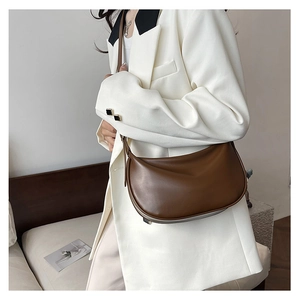 Brown faux leather crescent dumpling bag shown worn on shoulder with a white suit