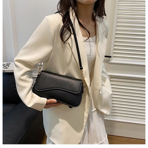 Détail du sac à bandoulière noir minimaliste avec rabat ondulé et anneau doré