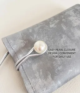 Detail of silver textured mini bag with white faux pearl button and elastic closure