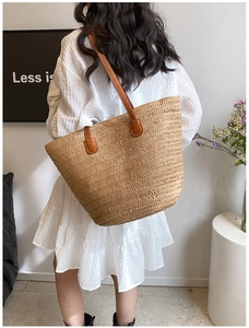 Detail of hand-woven straw tote with brown leather handles worn by woman in white dress
