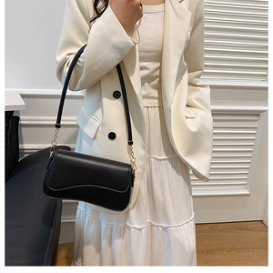Gros plan du sac sous le bras noir avec chaîne dorée sur une tenue de blazer blanc