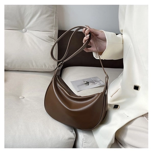 Detail of soft dark brown PU leather half-moon bag with smooth zipper on a sofa