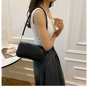 Détail du sac à bandoulière en cuir noir avec motifs ondulés sur un mur blanc