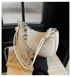 Close-up of white crescent bag featuring textured leather and pearl heart chain