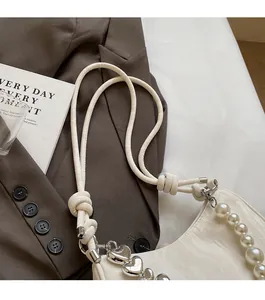 Detail of off-white underarm bag featuring heart metal chain and large pearl handle