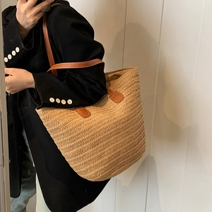 Minimalist straw tote bag with brown leather straps shown on a model for beach vacation
