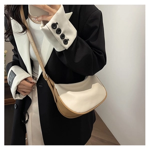 Detail of a chic two-tone cream and tan PU leather crescent bag worn by a model