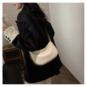 Side view of white faux leather crescent bag with brown trim on female model