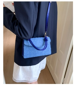 Detailed side view of blue denim crossbody bag with textured dots and knotted leather handle