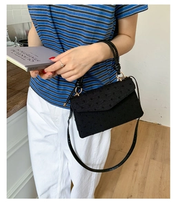Close-up of black crossbody bag with ostrich leather texture on casual female outfit