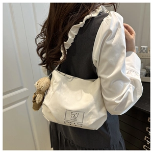 Detailed view of white canvas shoulder bag with ruffle strap and cute bear charm