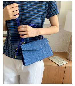 Close-up of blue denim flap bag featuring texture weave, gold hardware, and tassel detail