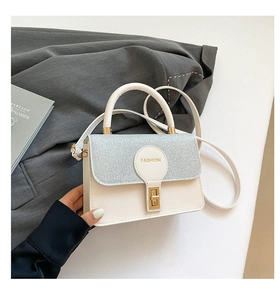 Detail of glitter flap and fashion logo on beige crossbody bag with gold lock closure