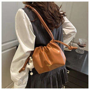Brown drawstring bucket bag with gold lettering shown on a model for scale and style