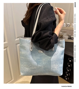 Detail of light blue denim tote bag featuring silver studs and metallic nameplate