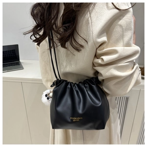Detailed close-up of a black pleated leather cloud bag with a cute white plush monster charm