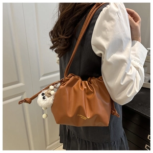 Detail of a brown pleated bucket bag with drawstring closure and a fuzzy monster charm