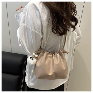 Detail of beige pleated cloud crossbody bag with gold text and plush monster charm decoration