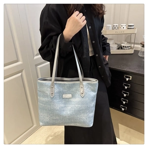 Detail of light blue glitter tote bag with silver logo plate on model's shoulder