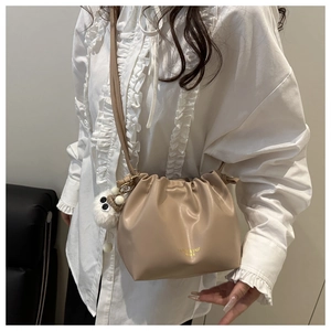 Detail view of a pleated beige leather bucket bag styled on a model with a plush charm