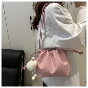 Detail of light pink drawstring bucket bag with leather texture and white pom-pom charm