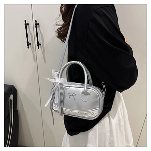 Detail of silver shell bag featuring metal bow badge and lace trim accents