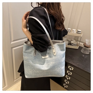 Detail view of light blue tote bag with silver leather handles and metallic brand logo
